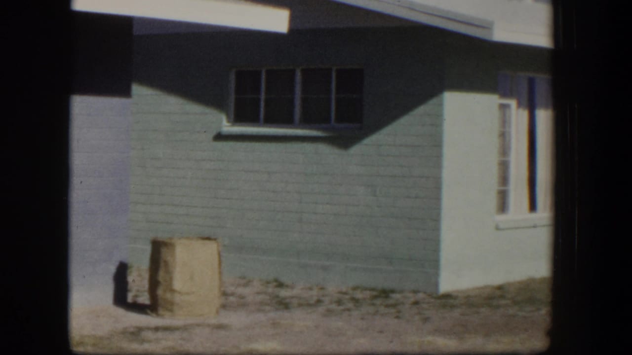 Light blue painted house wall with windows and a paper bag on dusty ground.