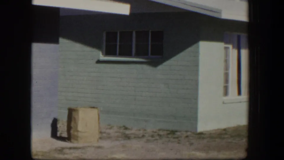 1954 Nevada frame of a freshly painted light blue house exterior with white trim, shadows, and a paper bag near the wall.