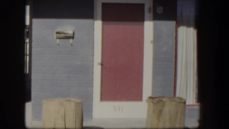 1954 Nevada 8mm frame showing a red residential door marked 331, gray block wall, white trim, mailbox, and tan containers.