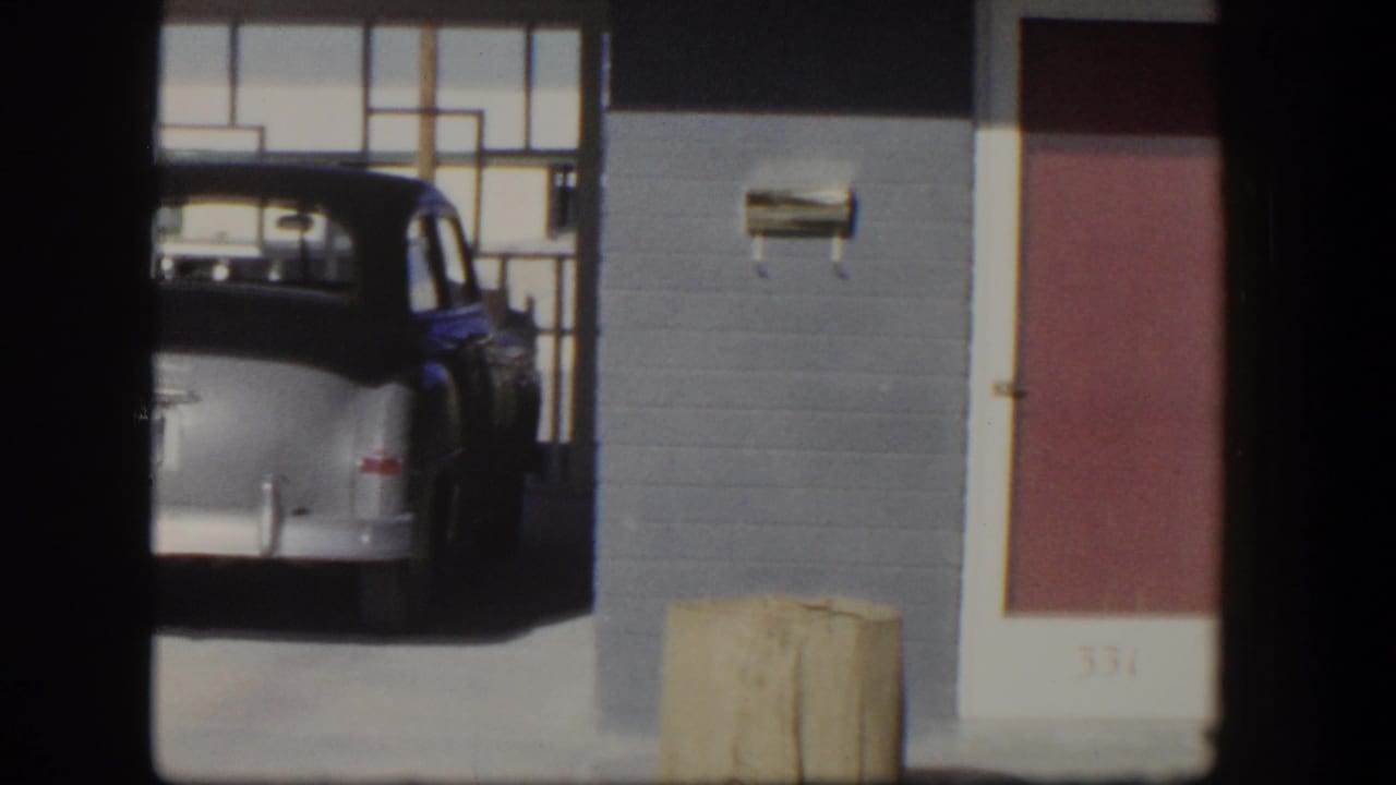 1954 Nevada home-movie frame showing a rounded older car near a brick storefront, broad windows, and a red door marked 331.
