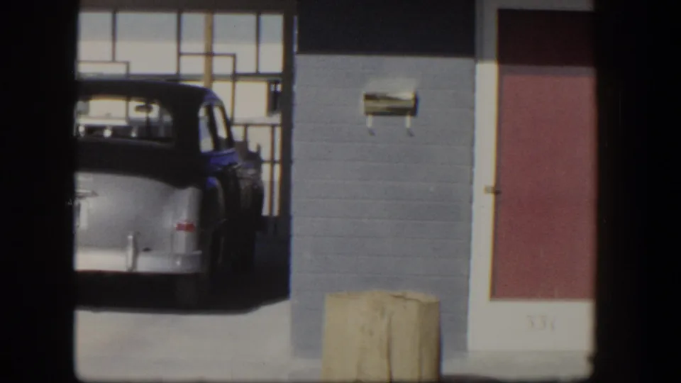 1954 Nevada home-movie frame showing a rounded older car near a brick storefront, broad windows, and a red door marked 331.