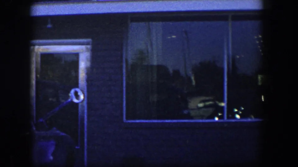 Blue-tinted 1954 Nevada frame of the storefront at night, with a glass door, large display window, reflections, and dark film borders.