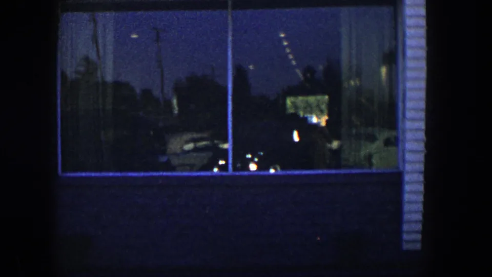 Nighttime 1954 Nevada home-movie frame showing a large storefront window, brick wall, reflections, and a vertical building edge.