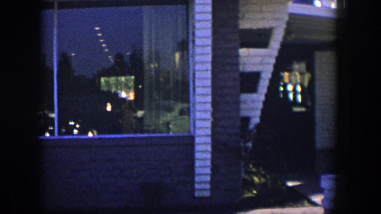 1954 Nevada home-movie frame showing a dim motel or hotel patio exterior with windows, stonework, and interior light reflections.