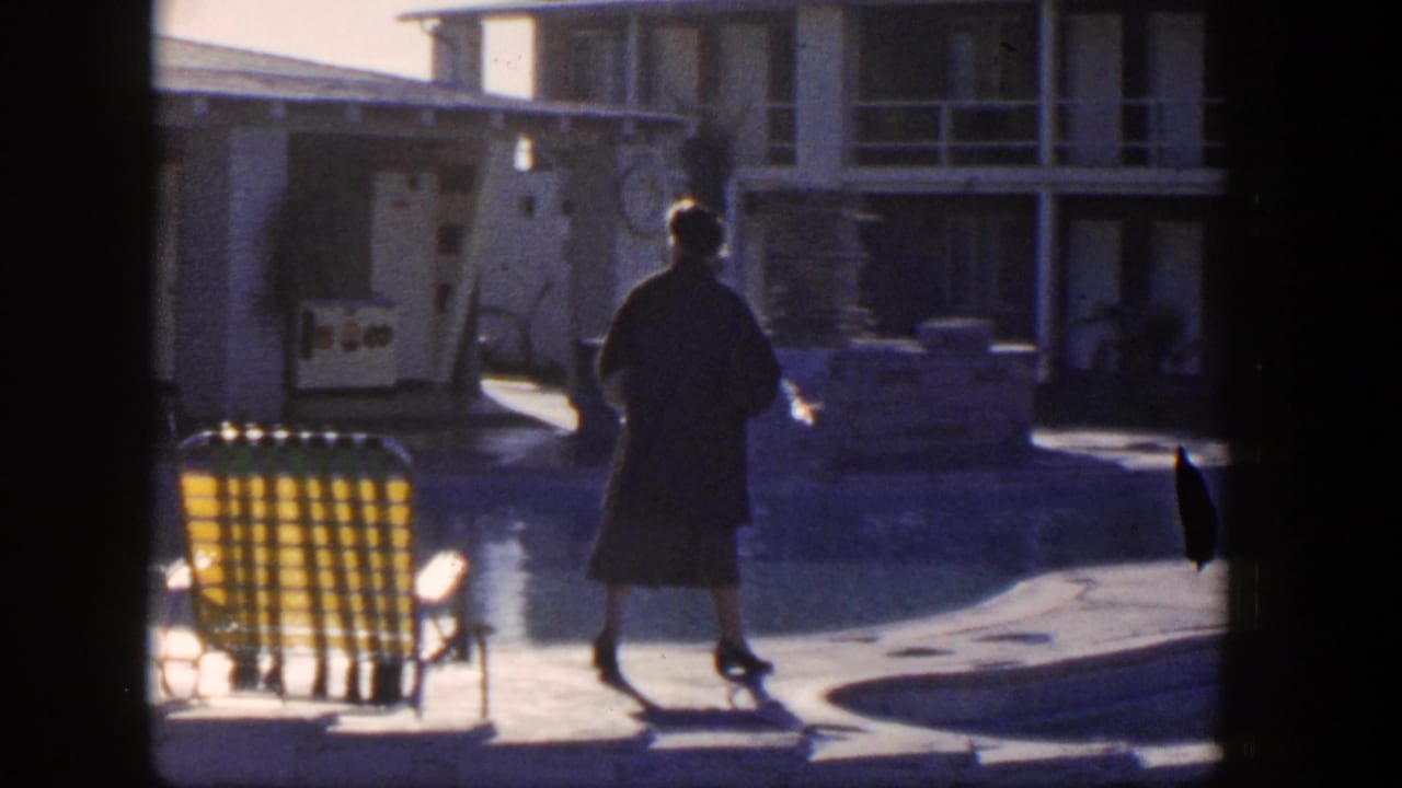 Woman walks along the pool deck with motel rooms and lounge chairs behind her.