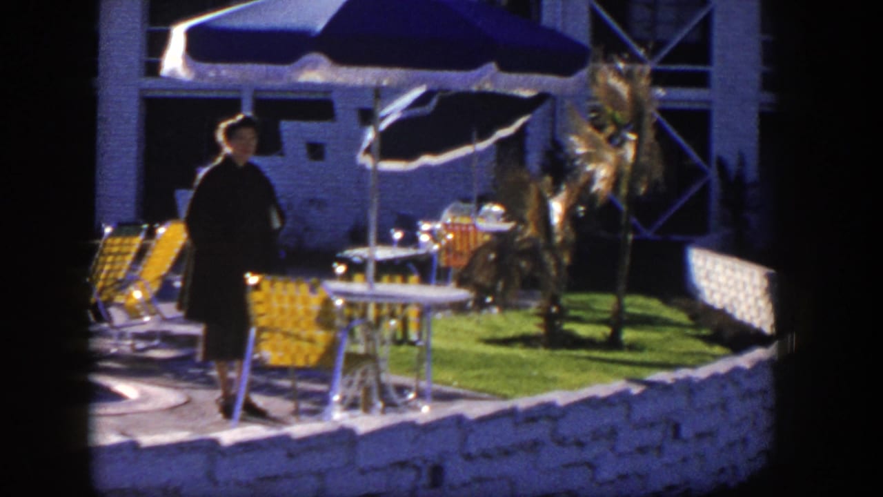 Woman standing near patio chairs, umbrellas, lawn, and white stone fence.