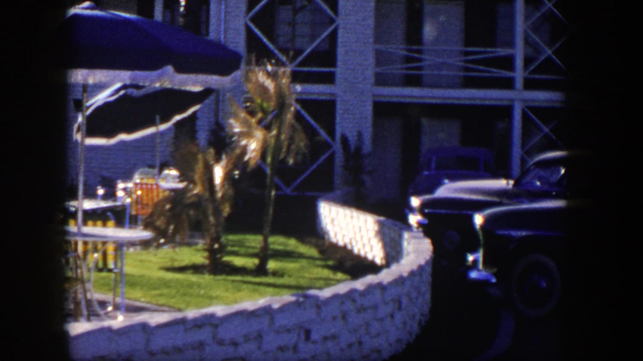 Patio umbrellas, lawn, stone fence, building facade, and parked dark car.
