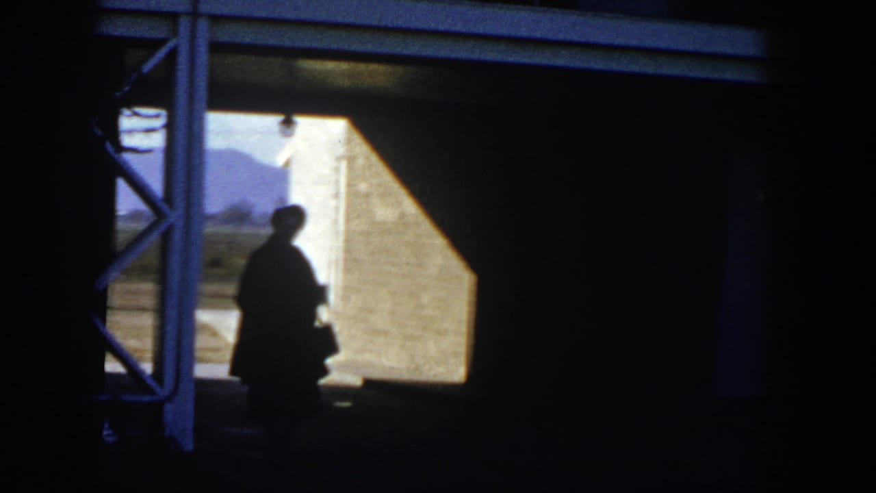 Silhouetted person stands in a shaded doorway facing bright sunlight.