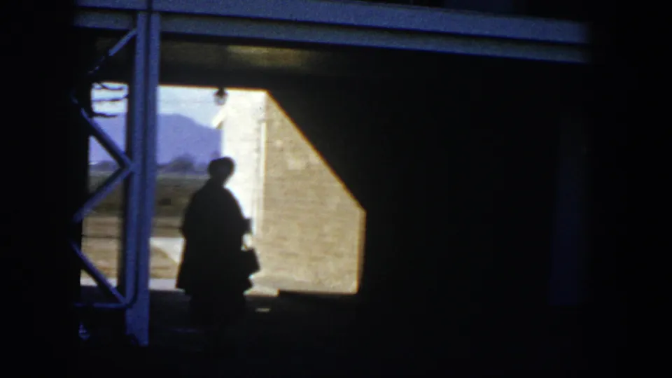 1954 Nevada 8mm frame with a silhouetted person in a hat at a doorway, backlit by bright desert sun.