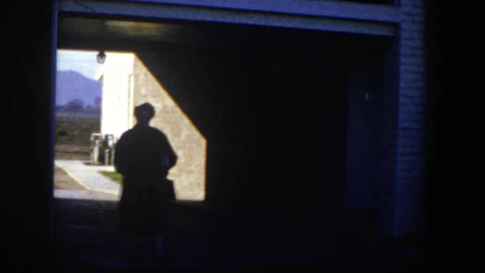 1954 Nevada 8mm frame showing a backlit person walking through a shaded passage into bright sunlight.