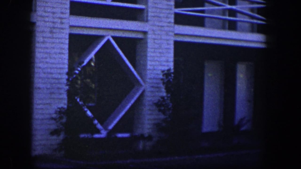 White brick exterior with diamond lattice detail, dark doorway or window, and shrubs.