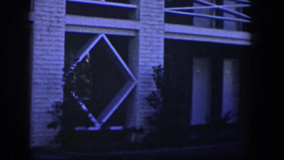 1954 Nevada exterior frame with a white brick wall, angled diamond lattice feature, dark recessed opening, and planted shrubs near the base.