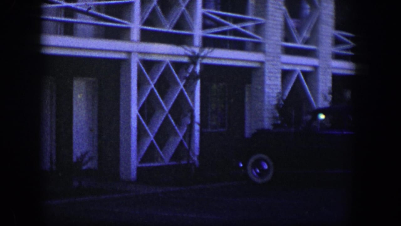 Dark sedan parked outside a two-story building with white geometric balcony rails.