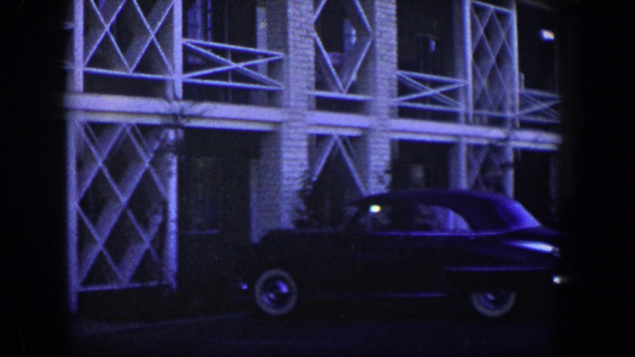 Classic sedan parked near a building facade with repeated white cross-braced railings.