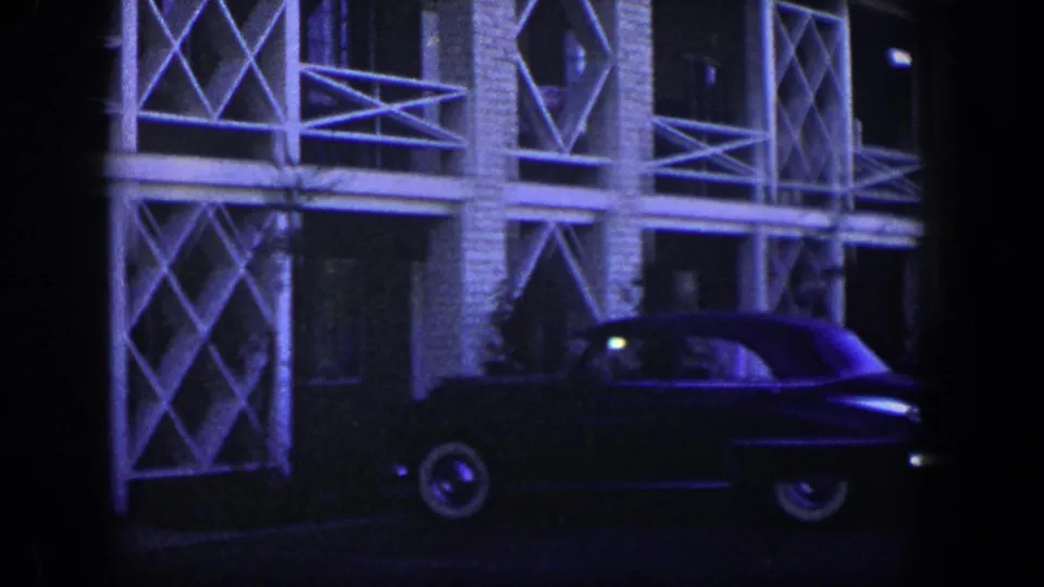 Dark 1950s sedan in front of a Nevada building facade with brick columns and white geometric balcony patterns.