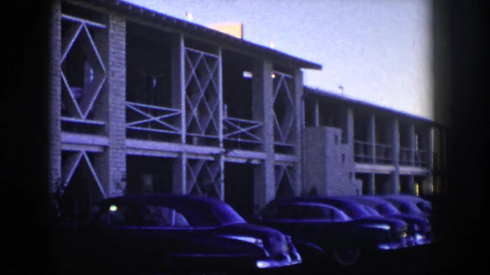 Wide 1954 Nevada frame showing several parked classic cars along a mid-century exterior with white cross-lattice railings.