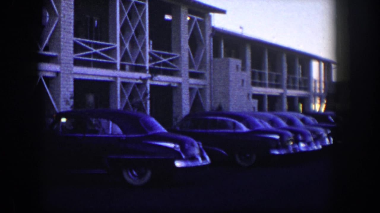 1954 Nevada 8mm frame showing parked mid-century cars in shadow beside a motel with cross-braced supports.