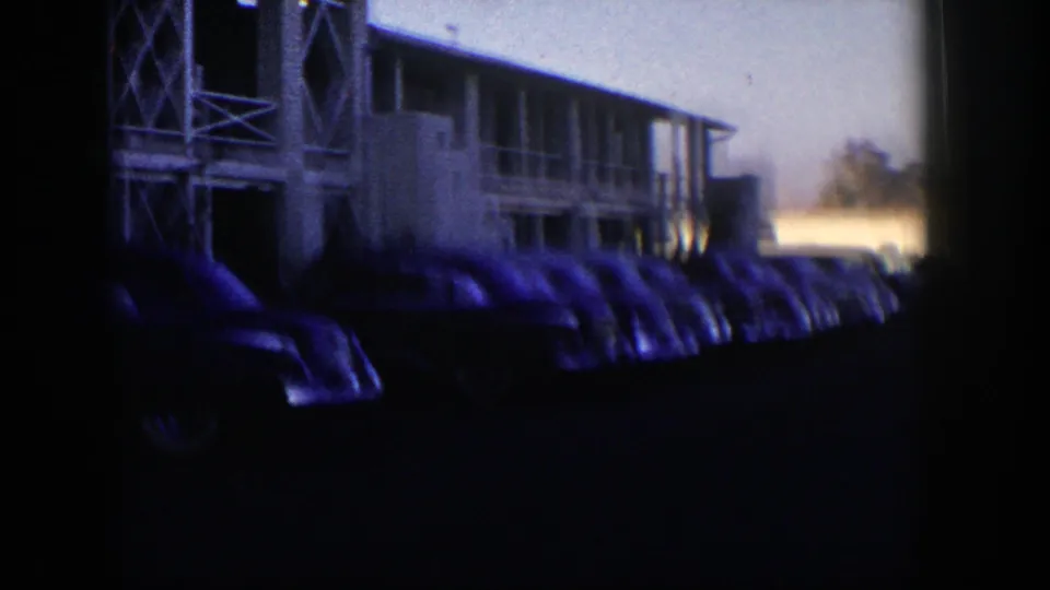 Soft 8mm frame of a Nevada motel parking area, with vintage cars and cross-braced supports partly obscured by shadow.