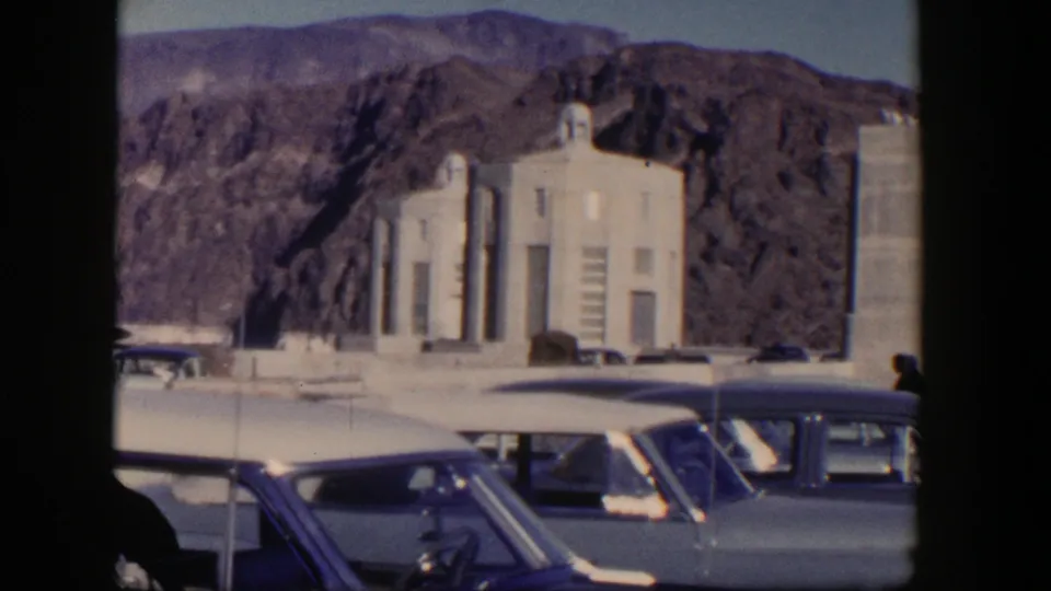 1954 Nevada frame showing parked cars before a pale building set against rocky desert hills, consistent with Hoover Dam area travel footage.