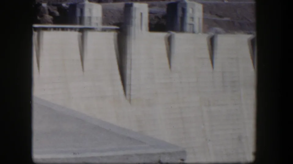 1954 Nevada 8mm frame of Hoover Dam's upper concrete wall, with geometric shadows and visible film-frame borders.
