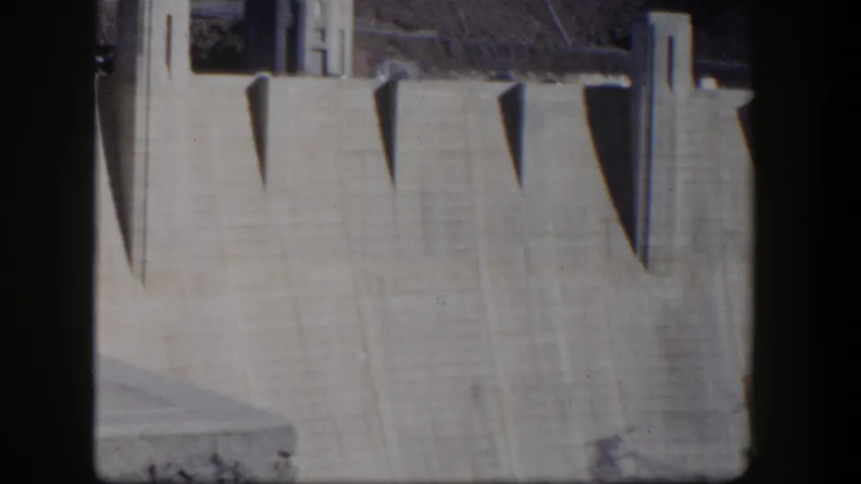 1954 Nevada 8mm frame showing a closer section of Hoover Dam's concrete wall, shadowed recesses, and cropped film edges.