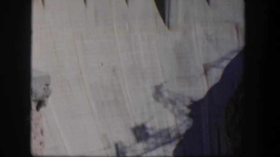 1954 Nevada 8mm frame of Hoover Dam's broad concrete face, with visible curvature, shadow, and a rocky edge near the lower right.