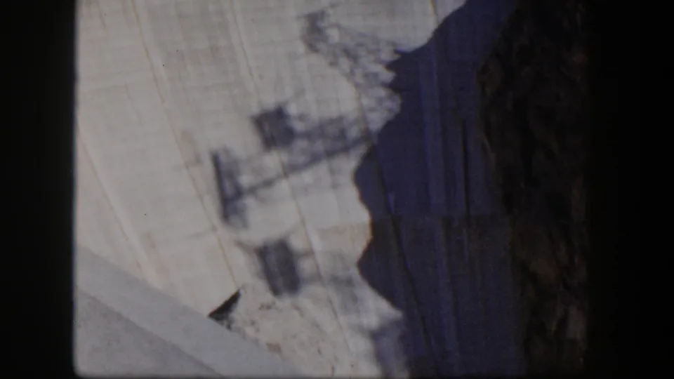 1954 Nevada frame with a pale stratified rock wall, dark vertical cliff edge, and indistinct foreground shadows.