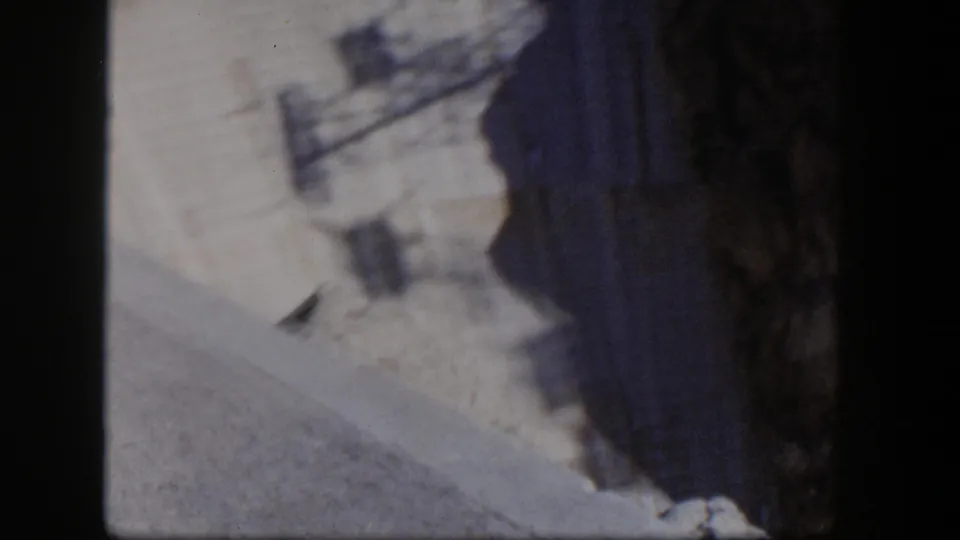 1954 Nevada home-movie frame showing a pale cliff face and dark rock mass from a low, unstable viewpoint.