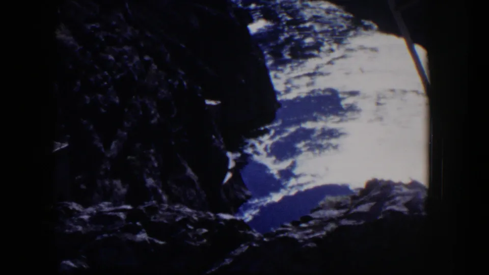 Late frame of the 1954 Nevada 8mm clip showing shadowed jagged rock, bright clouded sky, and partial metal framework.