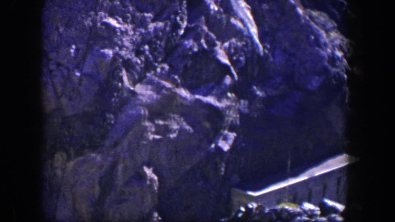 Dark blue-purple rocky cliff face with sparse brush and a pale ledge near the base.