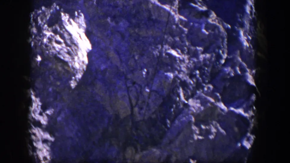 1954 Nevada 8mm frame showing rugged rock formations, bright exposed stone, shadowed crevices, and faint brush against the cliff.