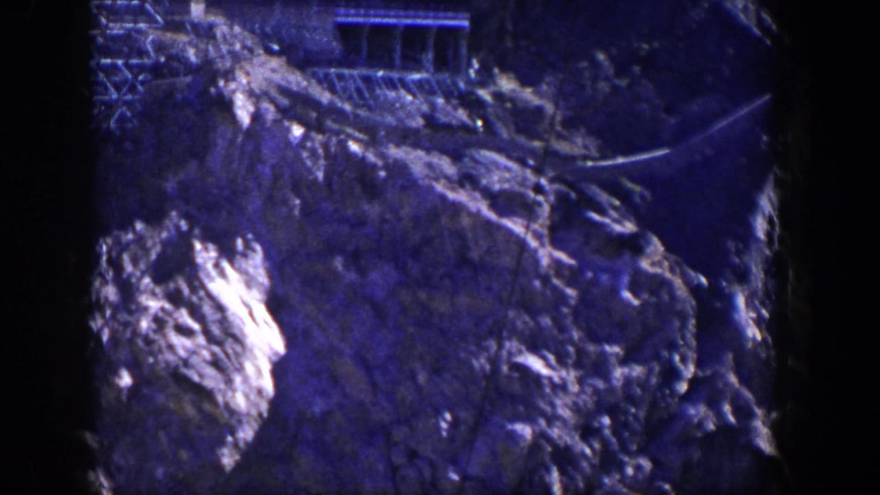 Rocky mountain slope with a small structure near the top and dark film borders.