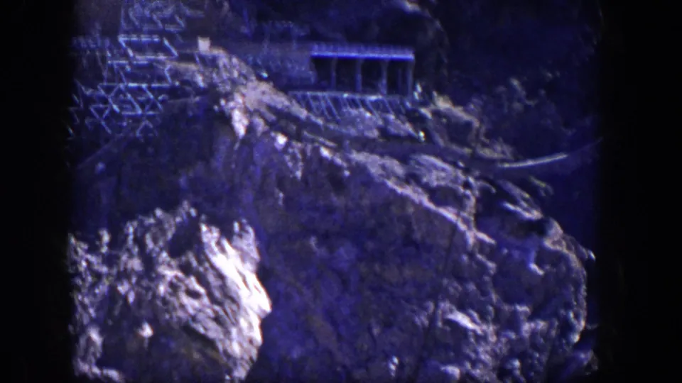 1954 Nevada home-movie frame of rugged rock below a slope-side structure and framework.