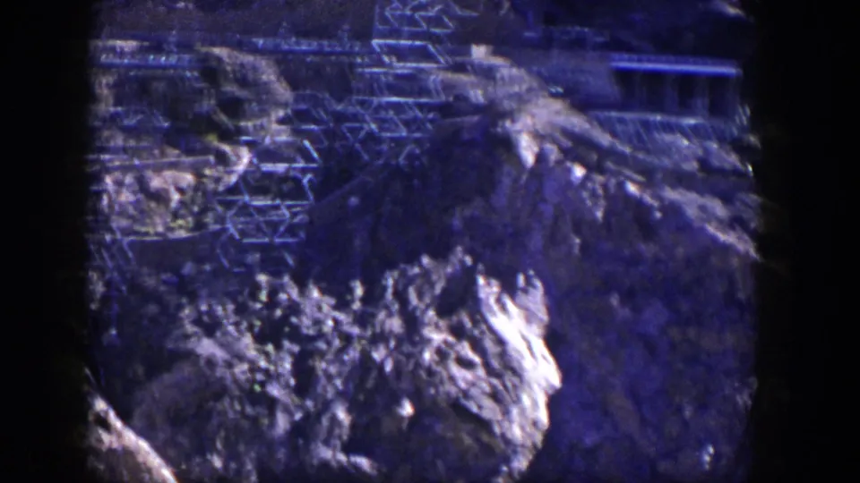 Blue-purple 8mm frame from Nevada showing rock formations and visible structural framework on the slope.