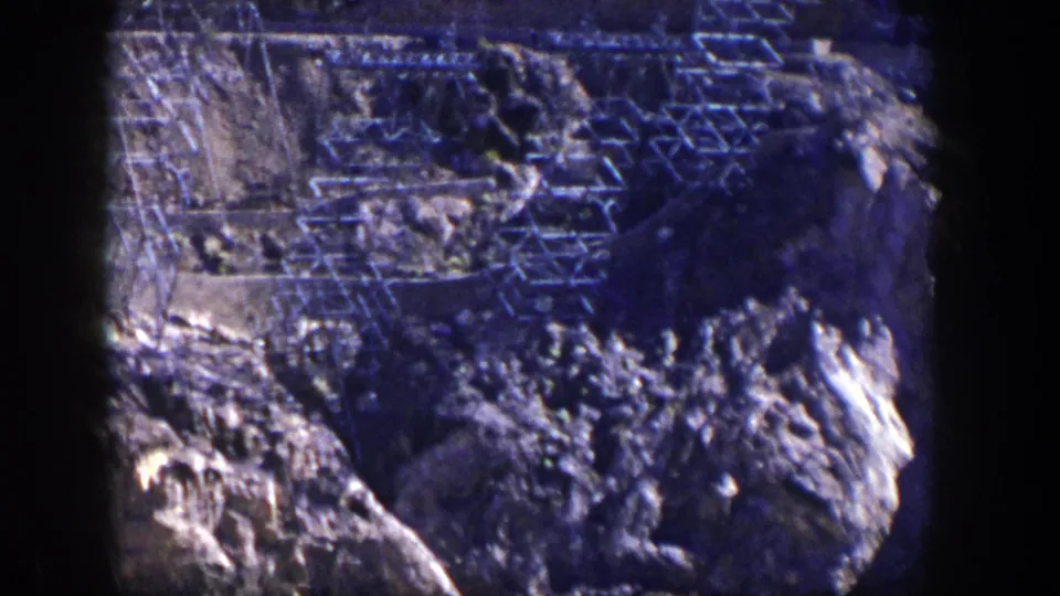 1954 Nevada 8mm frame showing a rugged hillside crossed by structural framework and sunlit rock.