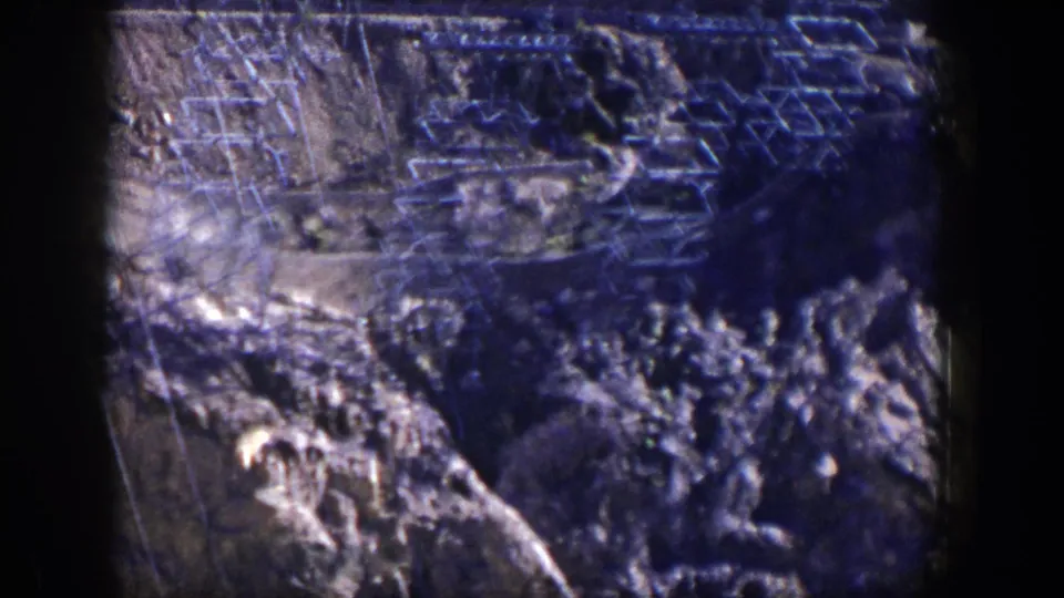 1954 Nevada 8mm frame showing electrical transmission towers and wires over tan rocks near Hoover Dam.