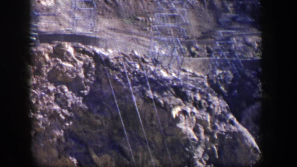 A handheld 8mm view of tan rocks, vertical power lines, and transmission structures near Hoover Dam in Nevada.