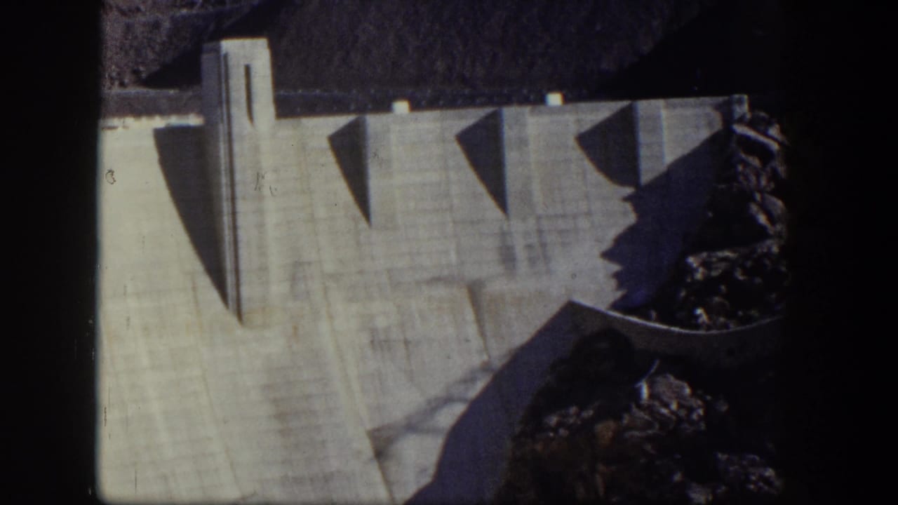 Concrete dam wall with a vertical tower and dark rock at the right edge.