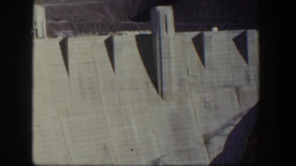 1954 Nevada 8mm frame showing the pale dam face and geometric shadows from projecting buttress forms.
