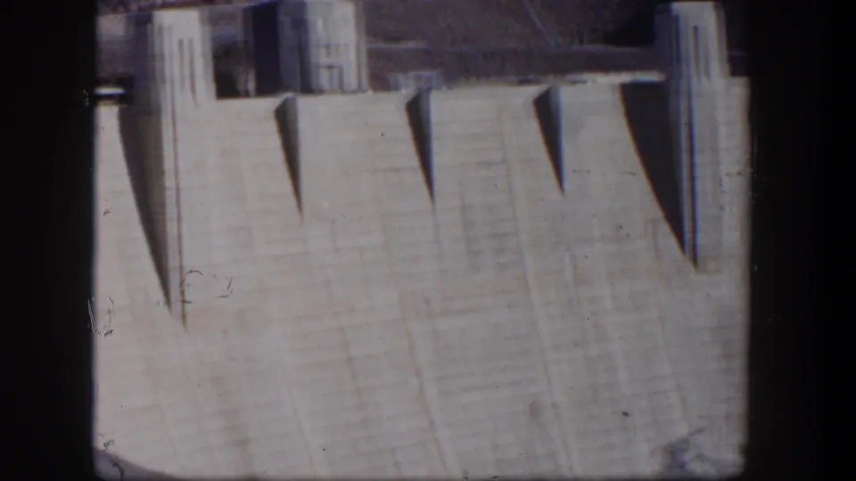 1954 Nevada 8mm frame of a sunlit concrete dam face in Nevada, with repeated geometric shadows and a tower-like element above.
