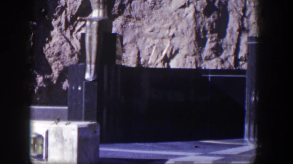 1954 Nevada frame showing the sculpture and rough rock backdrop above a dark structural base and sunlit ground.