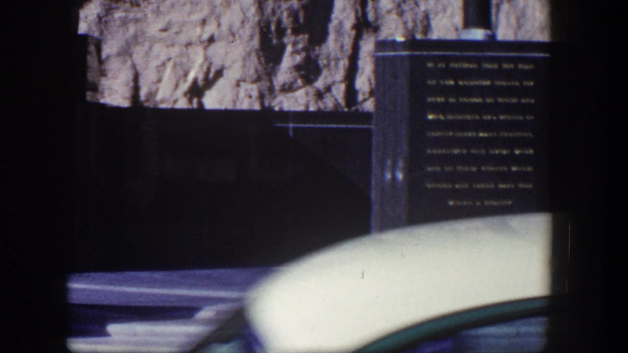 Engraved dark monument and rock face partly obscured by a white car in the foreground.
