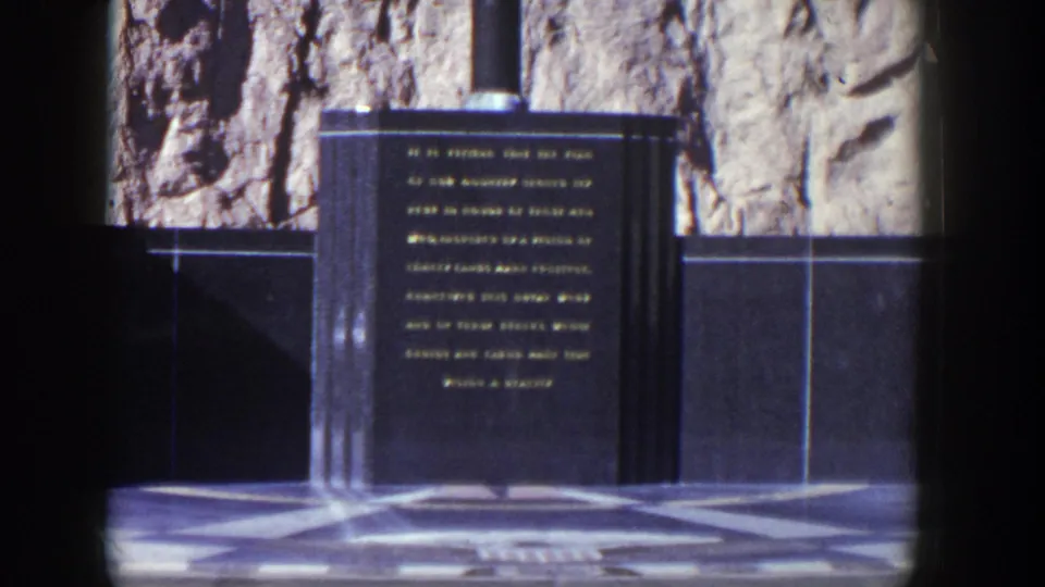 Late frame of the 1954 Nevada clip showing the engraved dark stone monument, vertical supports, black wall panels, and rocky background.