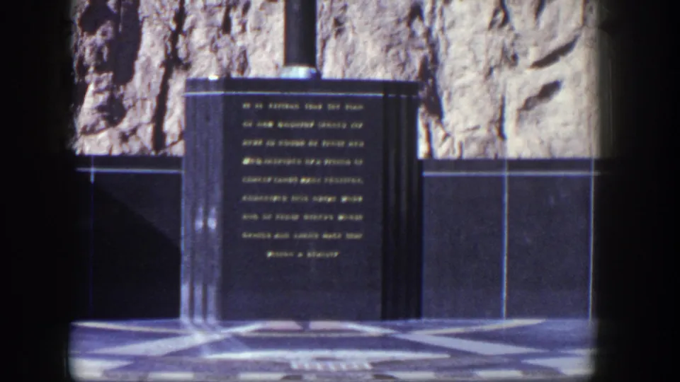 1954 Nevada 8mm frame showing a dark memorial inscription panel with gold text, tiled wall sections, and stone paving.