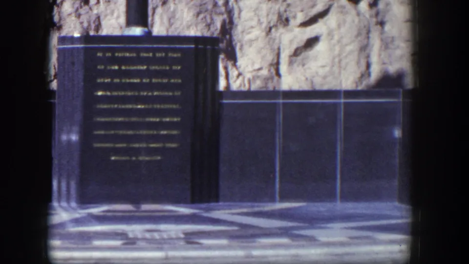 1954 Nevada 8mm frame centered on a polished black memorial panel with gold inscription and geometric paving below.