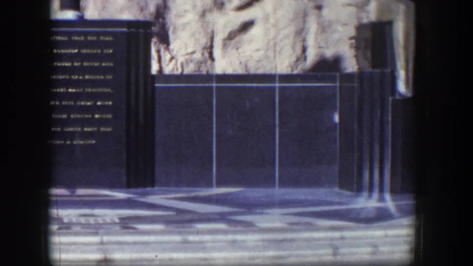 1954 Nevada 8mm frame showing the monument cropped at left, with tiled wall panels and patterned paving emphasized by the pan.