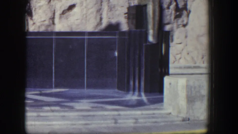 1954 Nevada 8mm frame showing the memorial structure's tiled wall, polished columns, rock backdrop, and stone base during the pan.