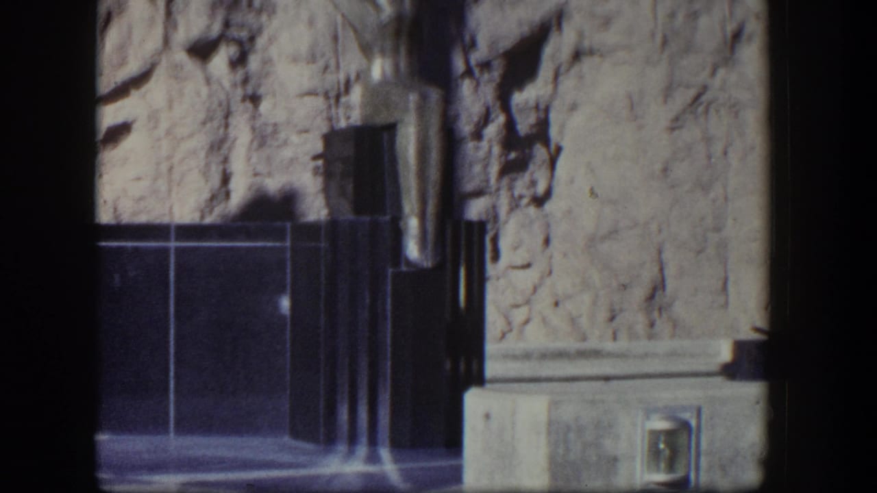 Dark monument base, rock wall, and lower portion of a winged sculpture.