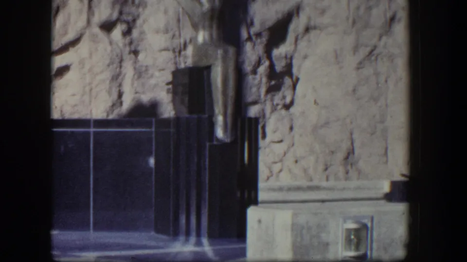 1954 Nevada frame with the Hoover Dam monument base, rough rock backdrop, and lower section of a winged figure at the edge of view.