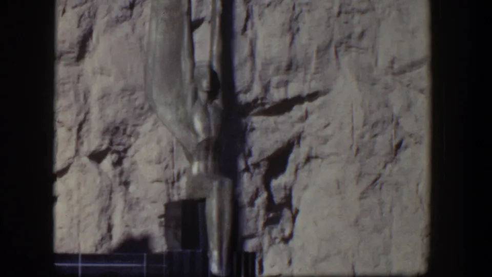 1954 Nevada frame showing the upper portion of a Hoover Dam winged figure sculpture set against a rugged rock wall.
